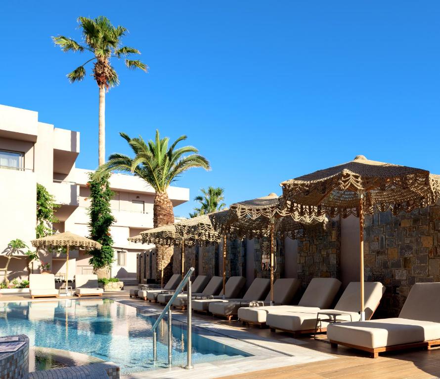 Vasaras kūrorta baseins ar sauļošanās krēsliem un palmām zem skaidras debess, radot relaksējošu atmosfēru.