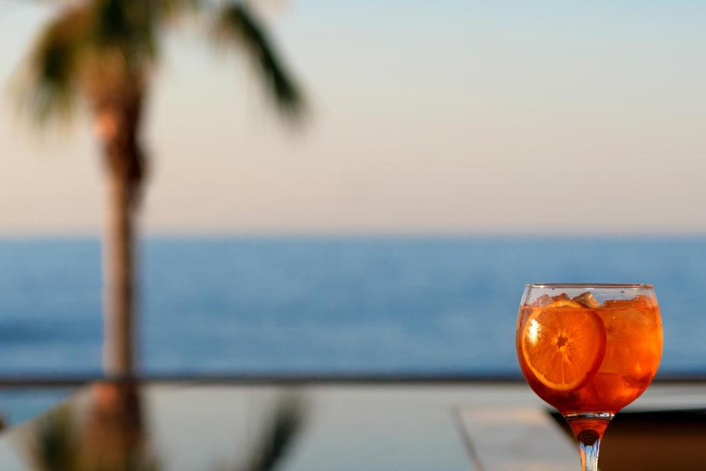 Kokteilis ar apelsīnu šķēlēm, stāvošs uz galda ar jūras skatu fonā. Ideāla atmosfēra atpūtai pie ūdens.