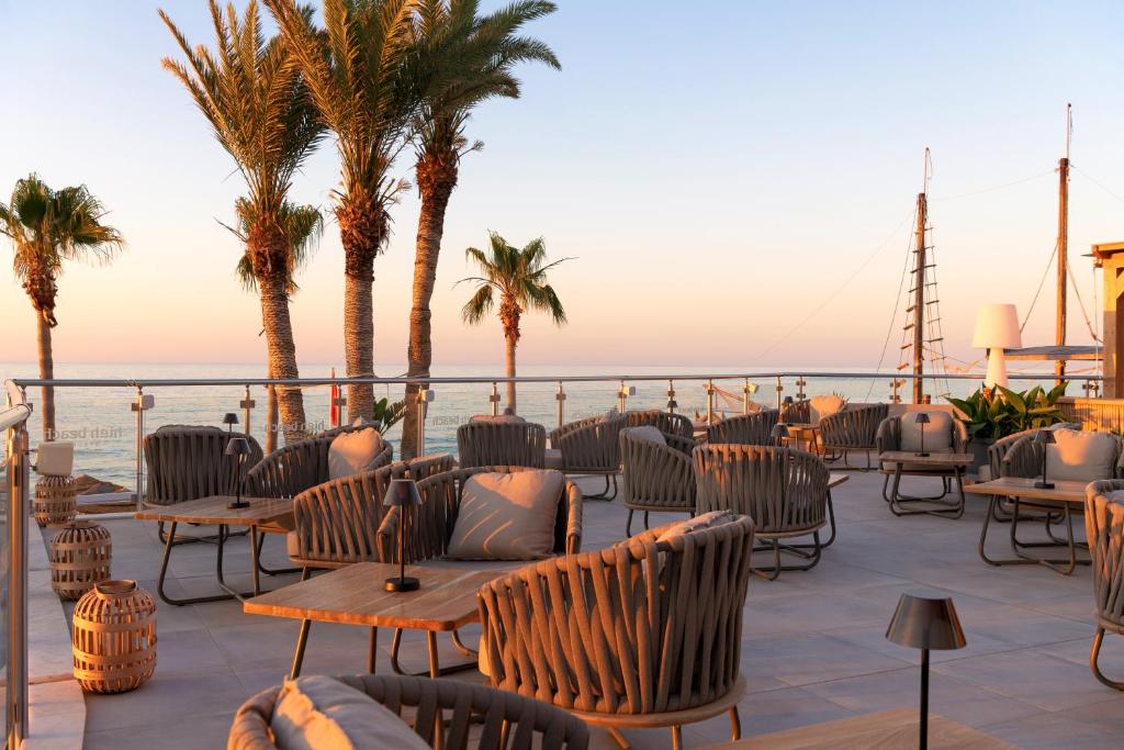 Skaisti terases skati ar palmām un jūras ainavu, kurā ir moderni sēdvietas un galdi, radot relaksējošu atmosfēru.