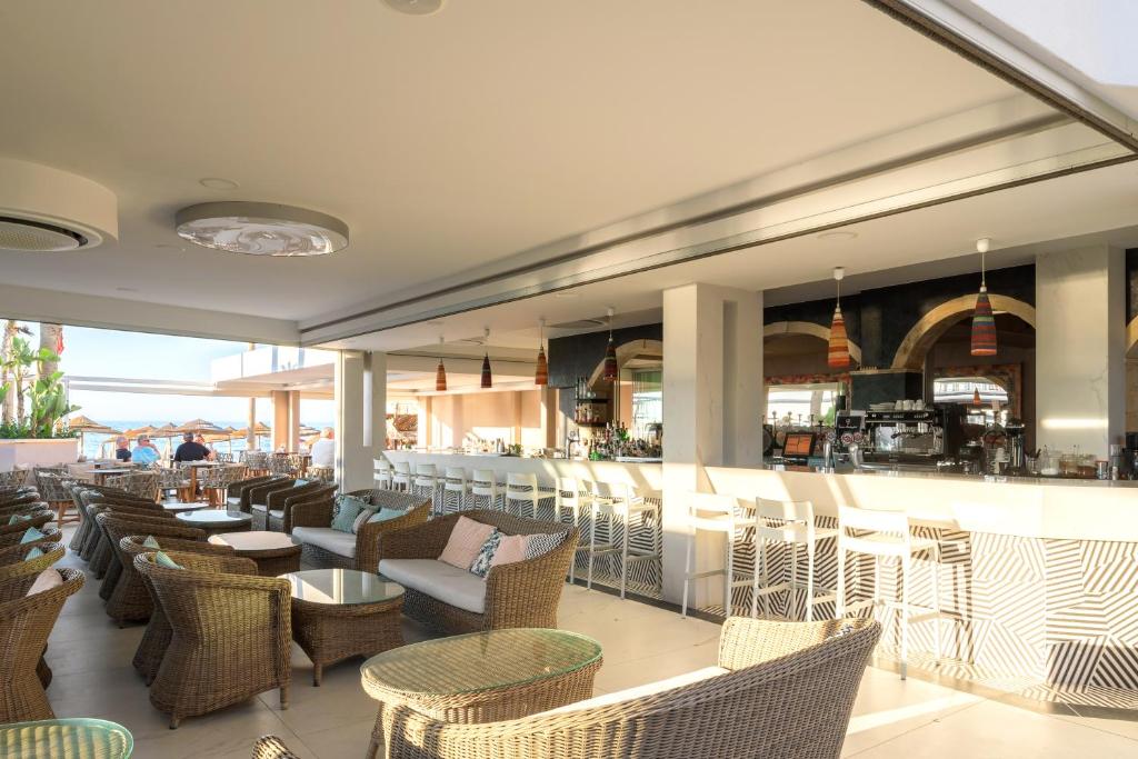 Moderns restorāns ar rattan mēbelēm un bāru, kas piedāvā skatu uz pludmali. Interjers ir gaišs un viesmīlīgs, radot relaksētu atmosfēru.