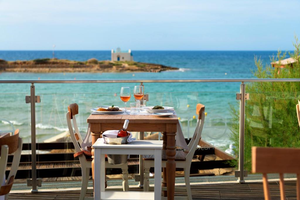 Jūras krastā esošs restorāns ar galdiem, uz kuriem ir ēdiens un dzērieni, piedāvā skaistu skatu uz mierīgu jūru un krastu.