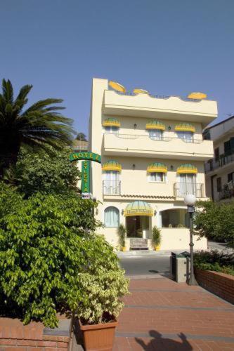 Viesnīca ar dzeltenām detaļām un zaļām palodzēm, ieskauta augiem un palmām, piedāvā viesmīlīgu atmosfēru un piekļuvi apkārtējai videi.