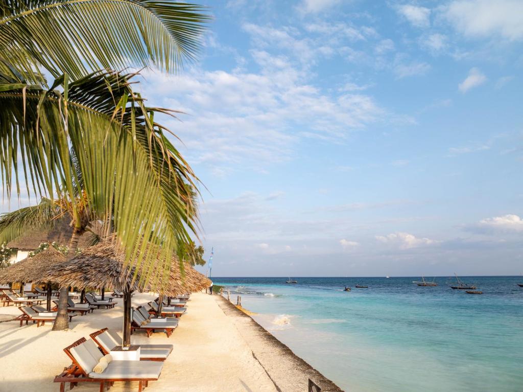 Pludmale pie Nungwi Beach Resort by Turaco ar palmām un saulessargiem.