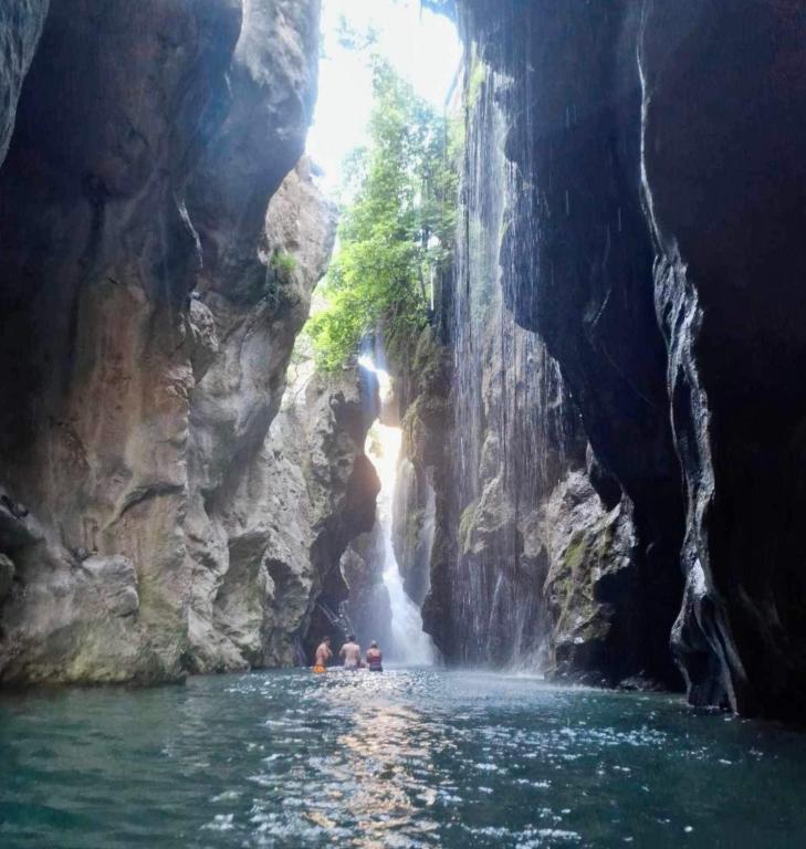 Dziļš kanjons ar krāšņu ūdens kritumu un cilvēkiem, kas peld ūdenī. Apkārtējās klintis ir apaugušas ar zaļām lapām, radot gleznainu ainavu.