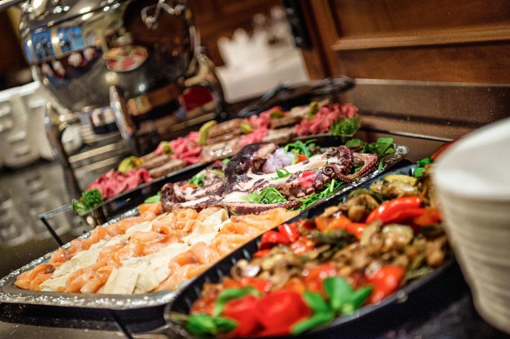 Svinību bufete ar dažādām gaļas un jūras produktu uzkodām, ieskaitot laša, gaļas un dārzeņu šķīvjus, grezni pasniegti ar zaļumiem un garnējumu.