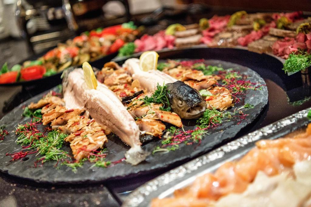 Svaigu jūras produktu plāksne, ietverot grilētu zivju, garneles un garšaugus, dekorēta ar citrona šķēlītēm un sarkano ziedlapiņu.