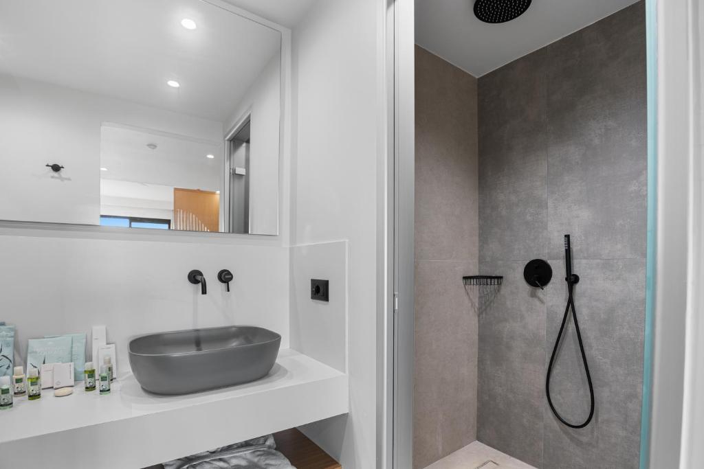 Mūsdienīgs vannas istabas interjers ar pelēku izlietni un dušas kabīni, kas iekārtota ar melniem aksesuāriem. Vannas istabā redzamas arī dabiskās kosmētikas līnijas pudelītes un liels spogulis.