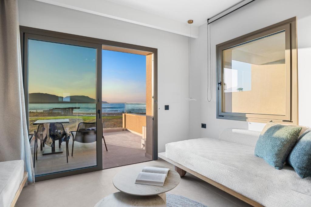 Mūsdienīgs interjers ar skatu uz pludmali un saulrietu, iekārtots ar ērtu dīvānu un galdu. Lielie logi nodrošina dabīgu apgaismojumu un piekļuvi ārējai terasei.