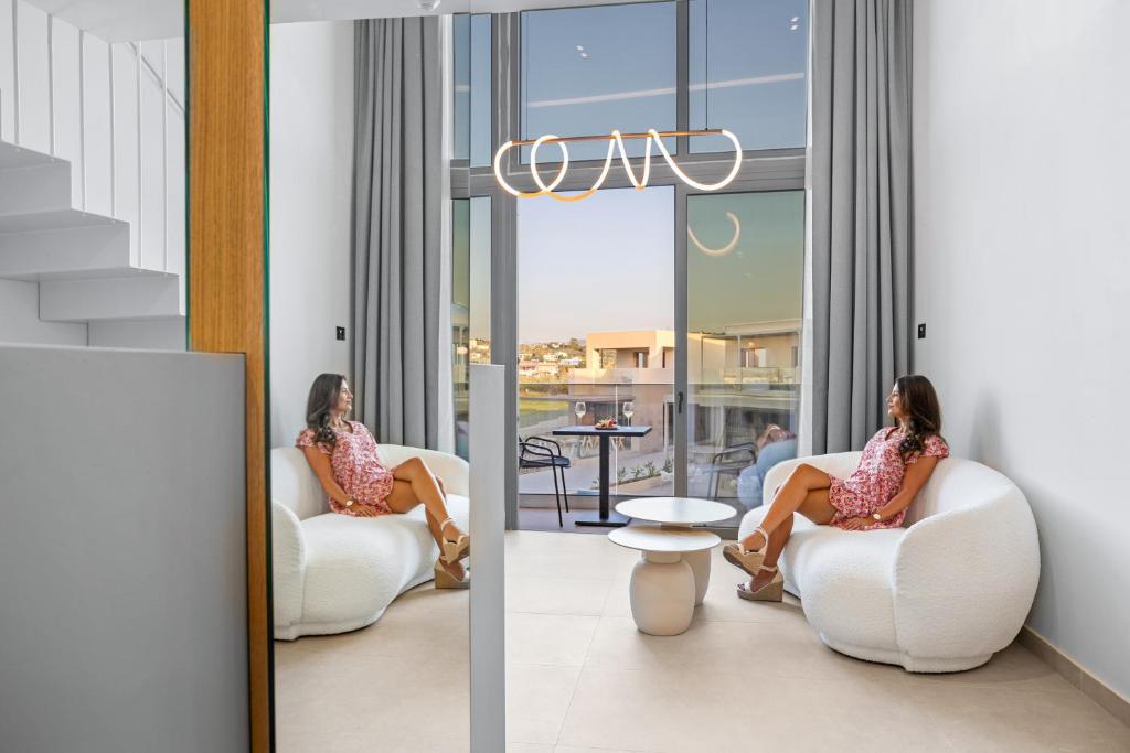 Mūsdienīgs interjers ar divām sievietēm, kas relaksējas uz ērtiem krēsliem, blakus logiem, caur kuriem redzama ainava. Telpa ir gaiša un stilīga, ar modernu apgaismojumu un minimālistisku dizainu.