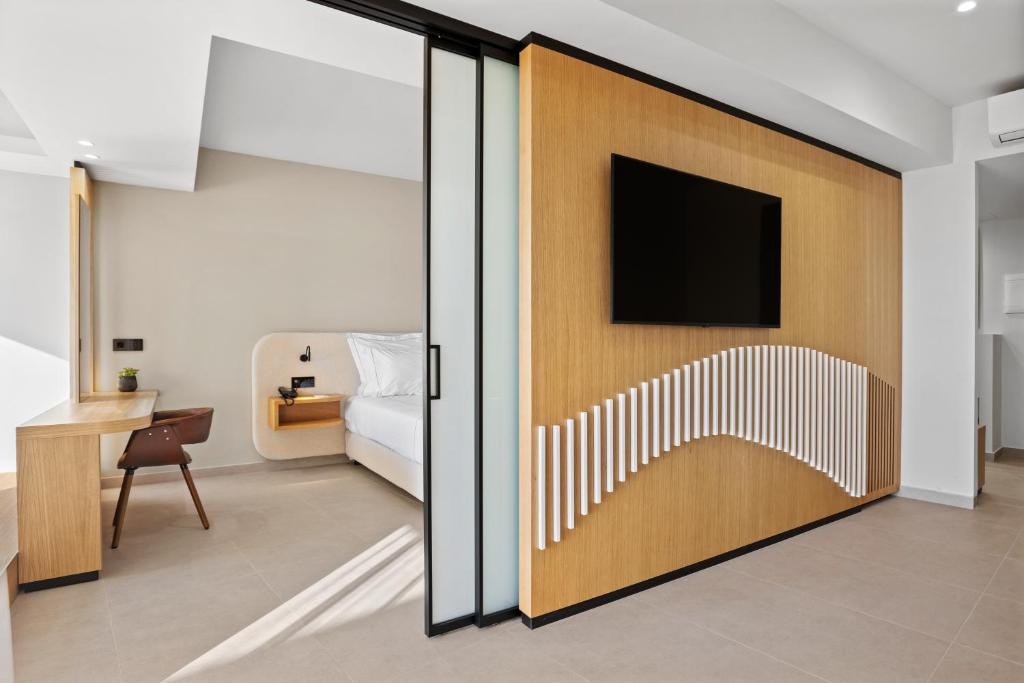 Mūsdienīga viesnīcas istaba ar koka akcentiem, stikla durvīm un plašu gultu, kurā ir televizors un rakstāmgalds. Eleganti interjera elementi nodrošina komfortu un stilu.