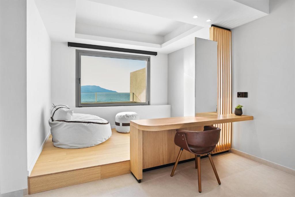 Mūsdienīga telpa ar skatu uz jūru, kurā ir koka galds, krēsls un komfortabla sēžammaiss. Interjers ir gaišs un minimālistisks, radot mierīgu atmosfēru.