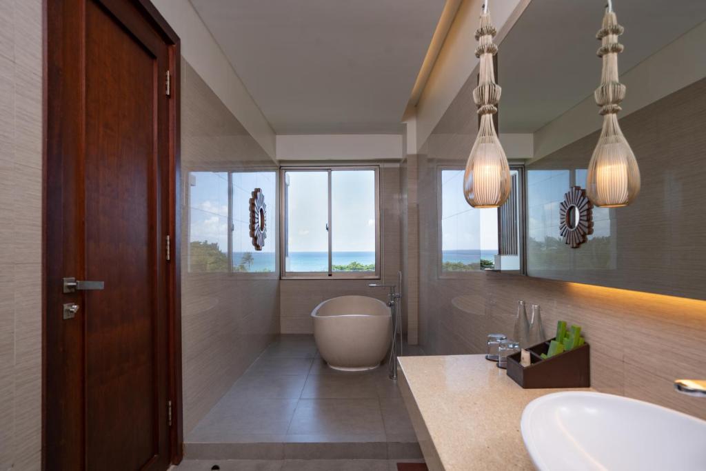 Moderns vannas istabas interjers ar lieliem logiem, kas sniedz skatu uz jūru, elegantiem apgaismojuma ķermeņiem un mūsdienīgu vannu.