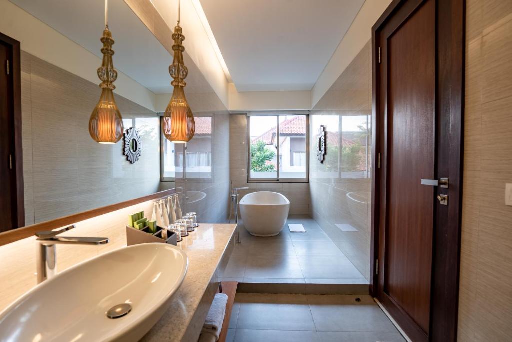 Mūsdienīga vannas istaba ar elegantu dizainu, kurā ir brīvstāvoša vanna, modernas izlietnes un lielas logu vienības, kas nodrošina dabīgu apgaismojumu. Interjers ir veidots ar neitrālām krāsām un dekoratīviem elementiem, radot relaksējošu atmosfēru.