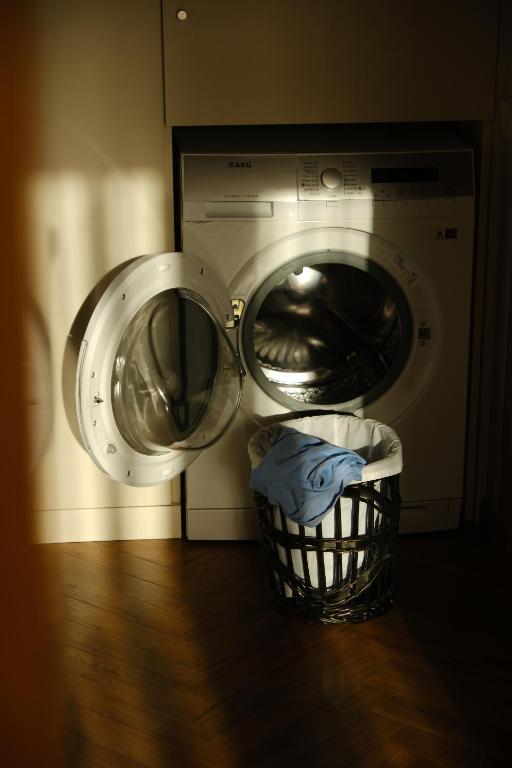 Veļas mašīna ar atvērtām durvīm un apakšā esošā veļas groza. Gaisma krīt uz mašīnu, radot mājīgu atmosfēru.