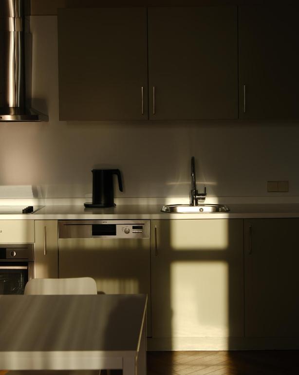 Mūsdienīga virtuve ar minimālisma dizainu, kurā redzams izlietne, elektriskais tējkanna un gaismas spēles uz virsmas.