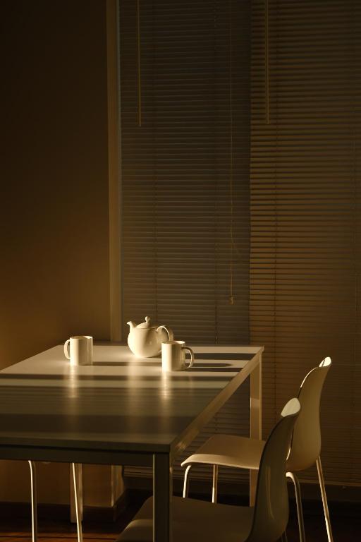 Gaiša un mierīga virtuve ar baltu galdu, uz kura atrodas tējkanna un divas krūzes, apgaismota ar maigu gaismu.