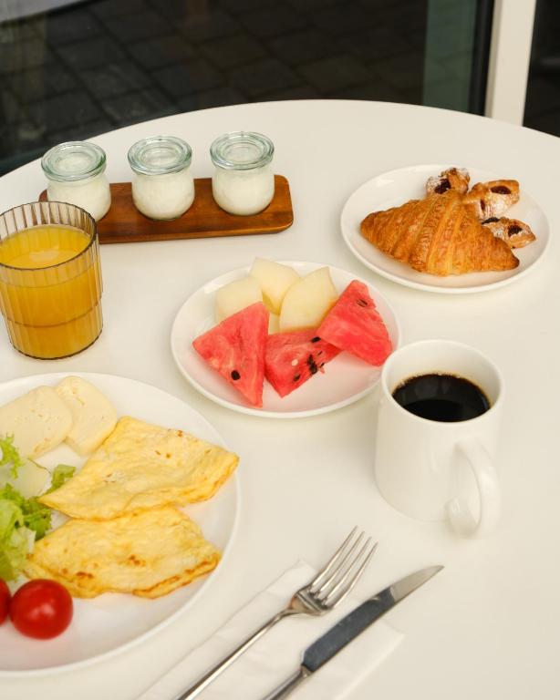 Broka veids ar omlete, svaigiem augļiem, kruasānu un kafiju, kas pasniegts uz baltas galda.