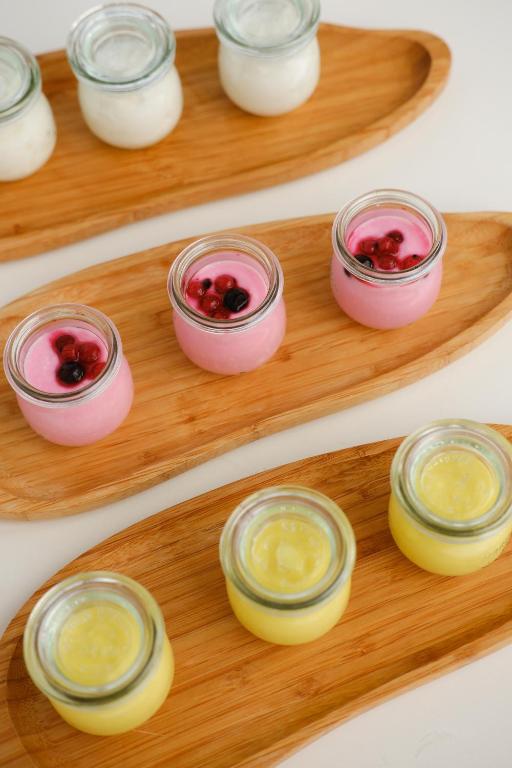 Krāsainu deserts burciņās, ieskaitot rozā, dzeltenu un baltu krēmu, kas pasniegti uz koka šķīvjiem. Ideāli piemērots ikdienas saldumu baudīšanai.