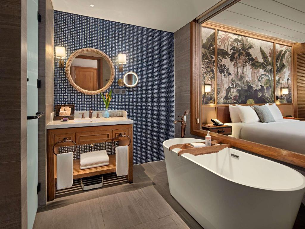 Moderns vannas istabas interjers ar elegantu brīvstāvošu vannu, koka izstrādājumiem un augu akcentiem. Sienas rotā stilīga flīžu mozaīka un augu motīvi.