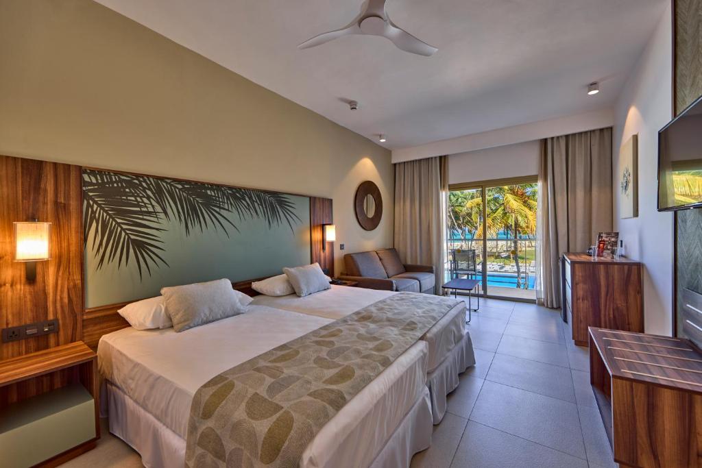 Moderns numurs ar divām gultām un skatu uz dārzu viesnīcā RIU Turquoise Mauritius.