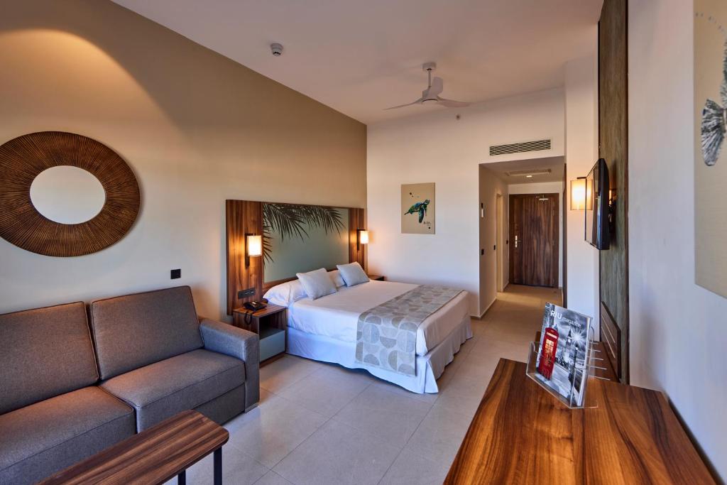 Mūsdienīgs numurs viesnīcā RIU Turquoise Mauritius ar dīvānu un TV.