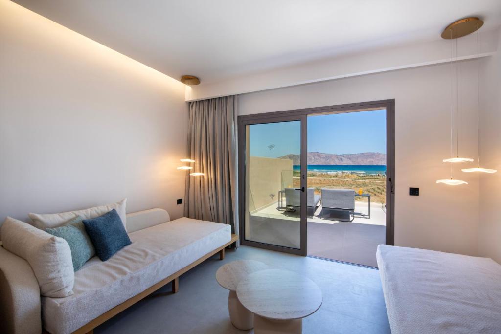 Mūsdienīgs viesistaba ar skatu uz jūru, gaišām krāsām un stilīgu mēbelēm. Telpā ir liels logs, kas nodrošina dabisko apgaismojumu un piekļuvi terasei.