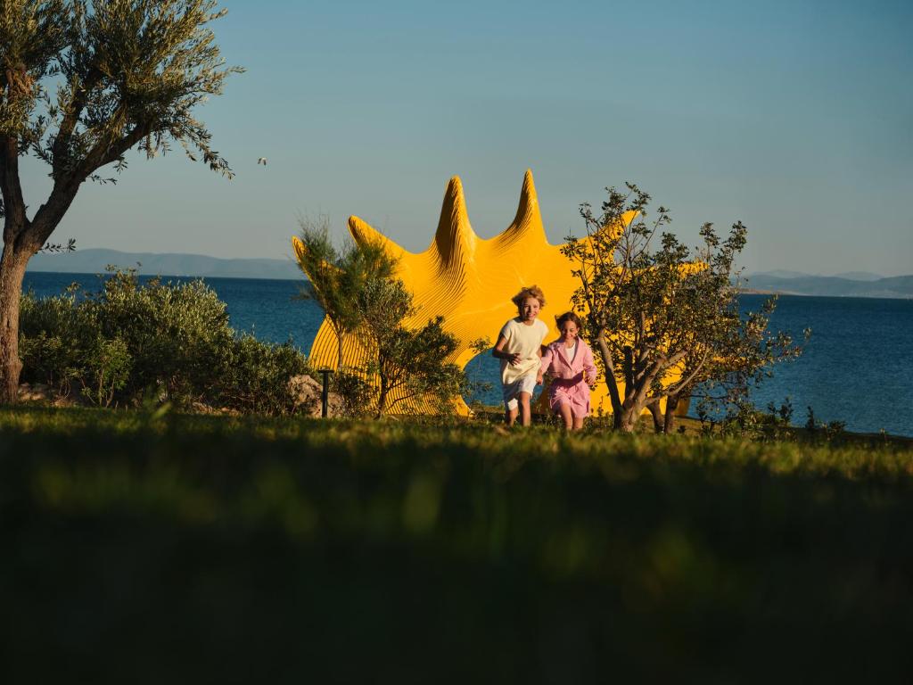 Bērni skraida pie Andas Barut Collection ar dzeltenu skulptūru fona.