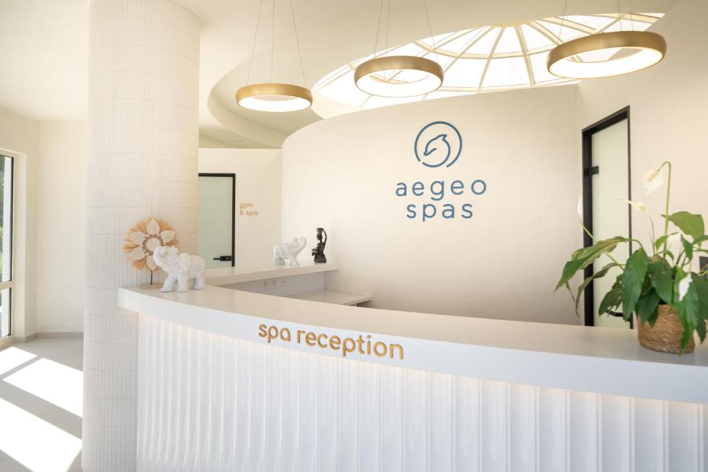 Moderns spa reģistratūras interjers ar gaišām krāsām, dekoratīviem elementiem un augu akcentiem. Redzams arī zīmols "aegeo spas".