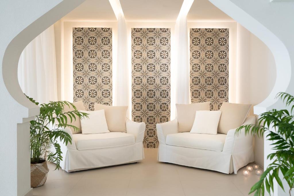 Mūsdienīgs interjers ar divām baltām dīvāna vietām un stilizētām, rakstainām sienām, kas radīs mājīgu atmosfēru. Telpā ir arī zaļas augu detaļas, pievienojot dabas elementus.