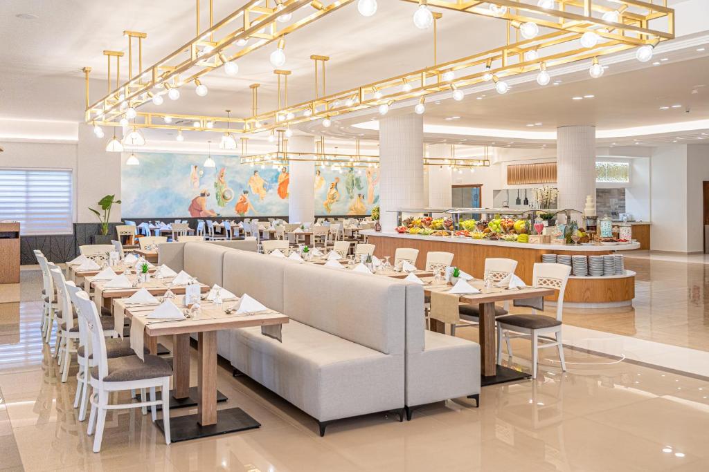 Mūsdienīgs restorāns ar gaišām interjera krāsām un elegantiem galdiem, kas rotāti ar galda piederumiem. Fons ir dekorēts ar gleznainu sienu, un redzama bagātīga ēdienu izvēle bufetē.