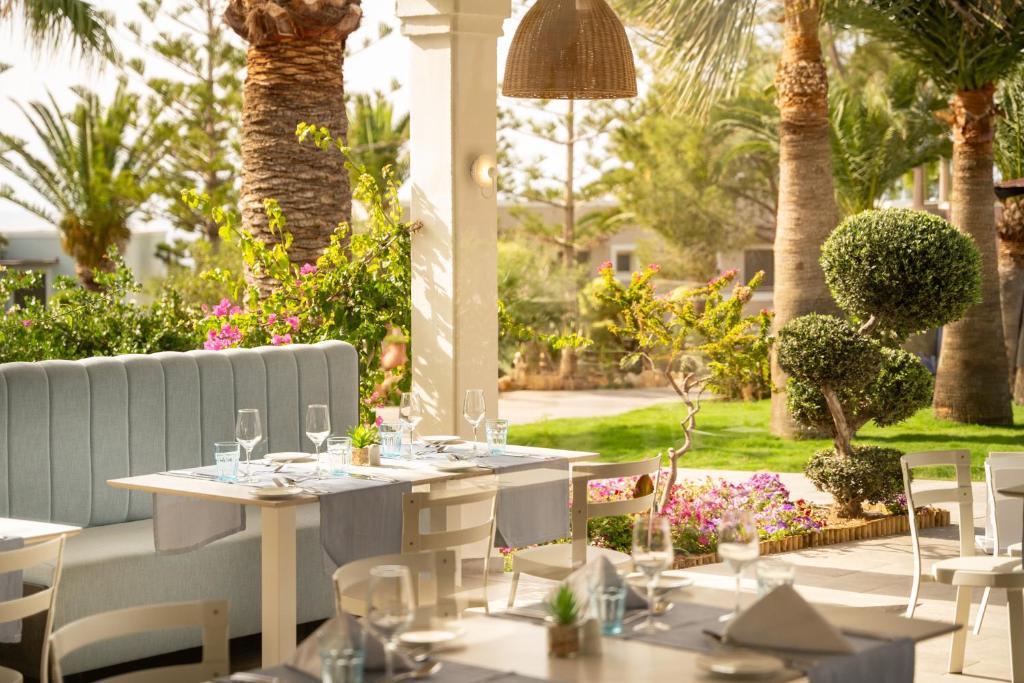 Skaista restorāna iekārtojuma aina ar zilu dīvānu un galdiem, apzaļumotu vidi un ziediem. Ideāla vieta atpūtai un ēdiena baudīšanai.