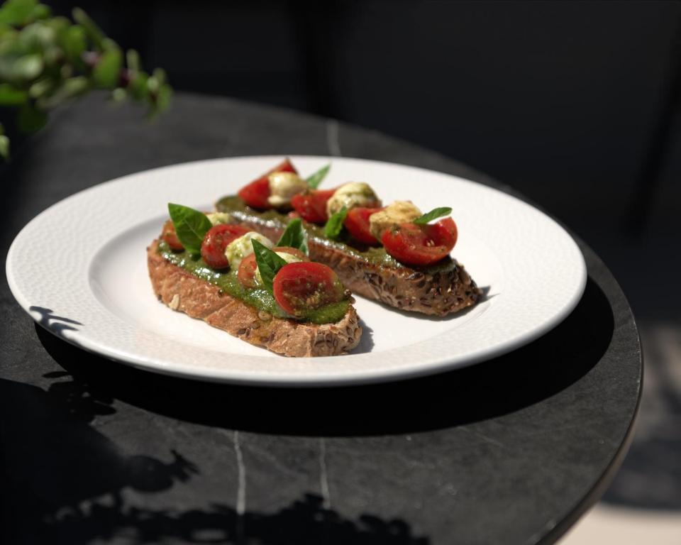 Svaigu grauzdiņu šķēles ar pesto, tomātiem un baziliku uz balta šķīvja, kas novietots uz melna galda.