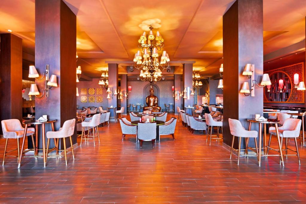 Elegants restorāns ar modernu interjeru, kurā ir izsmalcināti gaismas elementi un komfortabli sēdvietas. Centra daļā redzams Budas statuja, kas piešķir mierīgu atmosfēru.