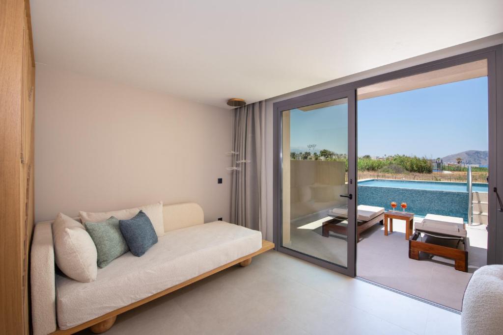 Mūsdienīgs viesnīcas numurs ar ērtu dīvānu un skatu uz baseinu ārpusē. Interjers ir gaišs un gaumīgs, radot relaksējošu atmosfēru.