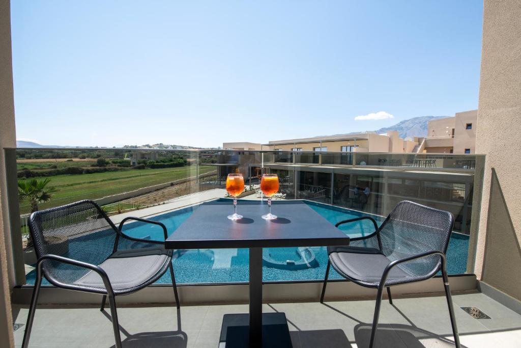 Balcony with a table and two chairs, featuring two glasses of a refreshing drink, overlooking a pool and scenic landscape. Perfect for relaxation and enjoying the view.