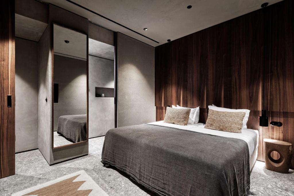 Mūsdienīgs guļamistabas interjers ar koka un betona elementiem, iekārtots ar divguļamo gultu un spoguli. Siltas krāsas akcenti rada relaksējošu atmosfēru.