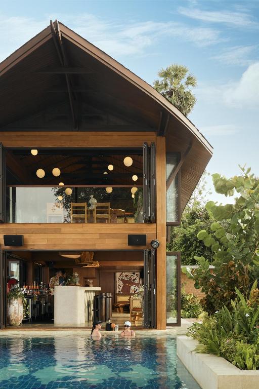 Mūsdienīga koka māja ar lieliem logiem un peldbaseinu priekšā, dekorēta ar zaļām augiem un ērtām mēbelēm. Ideāla vieta atpūtai un izklaidei.