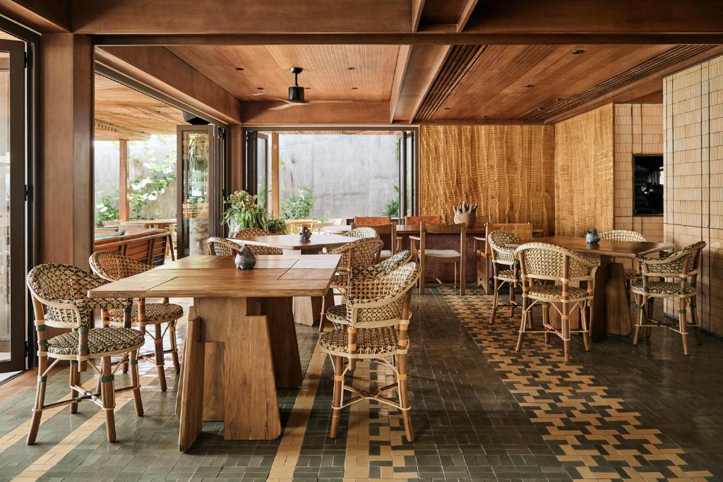 Mūsdienīgs restorāna interjers ar koka mēbelēm un džungļu elementiem, kas rada mājīgu atmosfēru. Atvērtas durvis nodrošina dabiskā apgaismojuma plūsmu un skatu uz zaļumu.