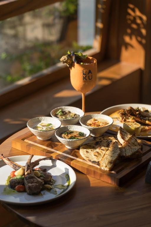 Elegants galda klājums ar dažādiem ēdieniem, tostarp zupām, gaļas porcijām un maizi, papildināts ar dzērienu. Gaismas plūst caur logiem, radot patīkamu atmosfēru.