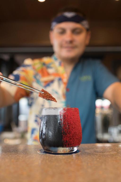 Kokteiļa pagatavošana ar čībām, kurš tiek pasniegts ar sarkanu dekoru uz stikla. Fons ir izplūdis, pievēršot uzmanību dzērienam.