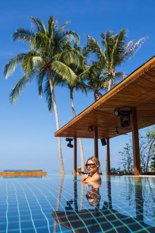 Sieviete atpūšas luksusa baseinā zem palmu kokiem ar skaidru zilu debesi.