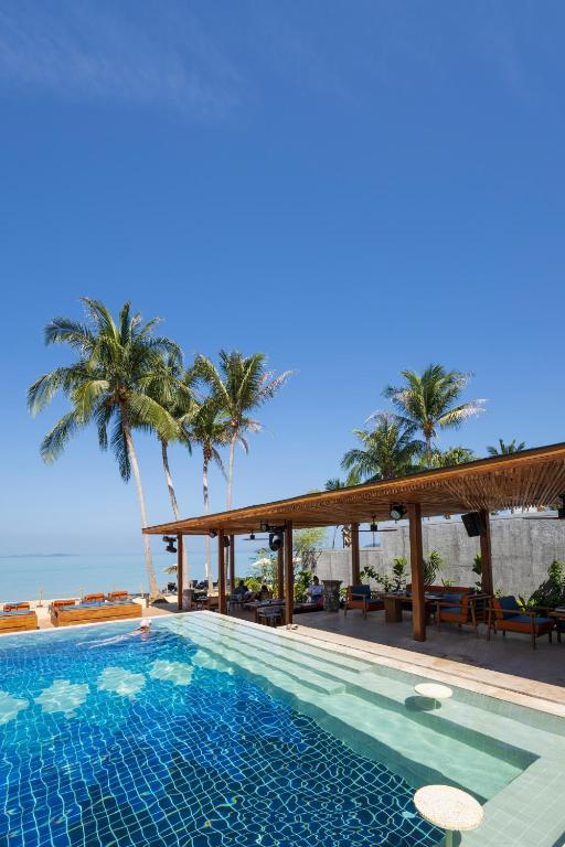 Peldbaseins ar zilām flīzēm un palmām, kas atrodas pie pludmales, ar skatu uz skaidro debesu un jūru. Relaksējoša atmosfēra, ideāla atpūtai.