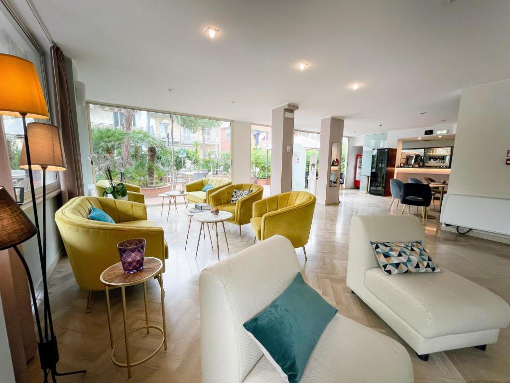 Mūsdienīgs viesnīcas interjers ar krāsainiem dīvāniem, gaišu apgaismojumu un plašām logu atverēm, kas piedāvā skatu uz ārējo dārzu.