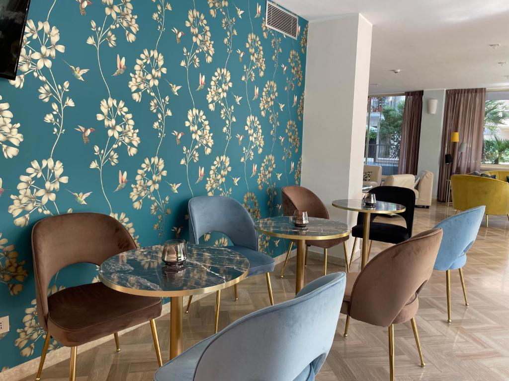 Mūsdienīgs kafejnīcas interjers ar zilu tapeti un elegantiem krēsliem, kas veidoti no dažādu krāsu auduma. Uz galdiem atrodas sveces, radot patīkamu atmosfēru.