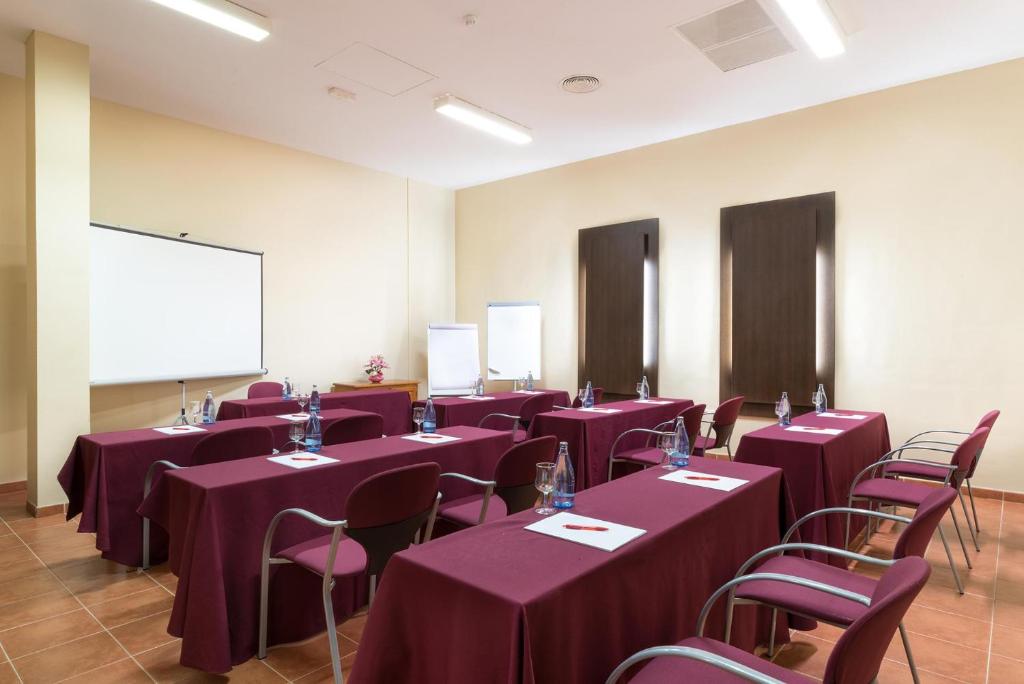 Konferenču telpa ar sarkaniem galdautiem un krēsliem, aprīkota ar projektoru un balto tāfeli. Telpa piemērota sanāksmēm un prezentācijām.
