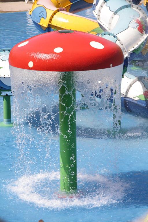 Krāsains ūdens atrakciju elements ar sarkanu sēņu formu un ūdens strūklām, kas plūst no tās apakšas. Ideāls bērnu ūdens parks vai izklaides vieta.