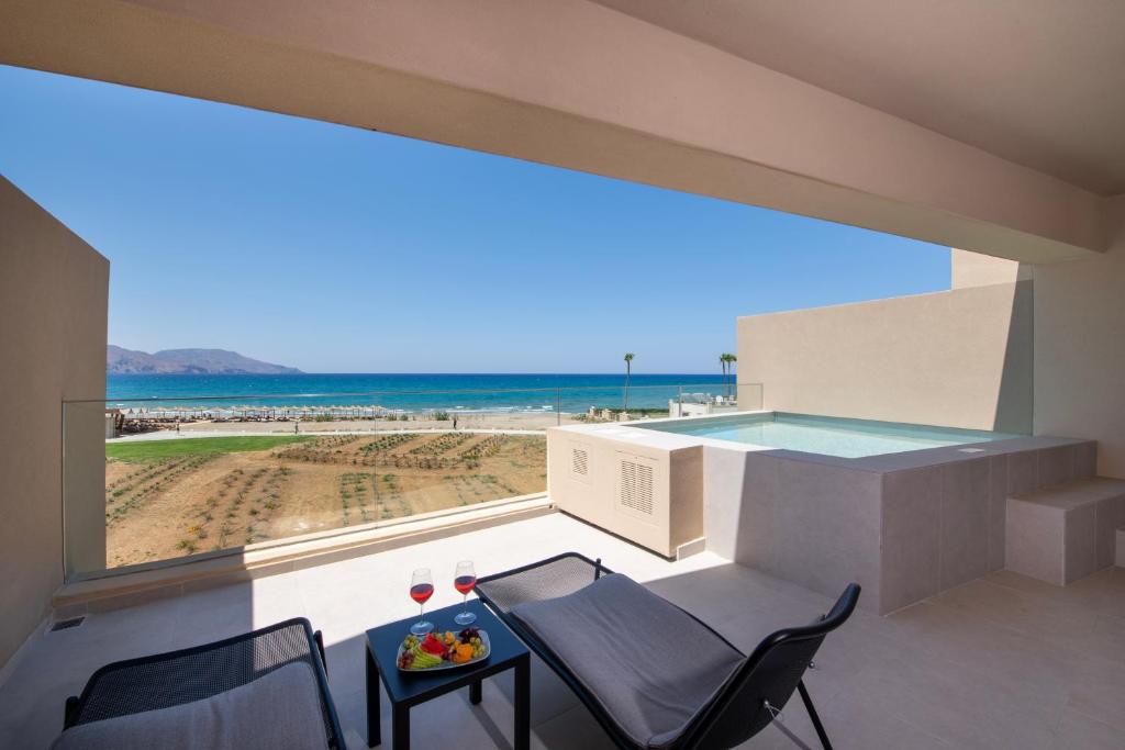 Mūsdienīgs balkons ar skatu uz jūru, divām ērtām krēsliem un dzērieniem, kas papildināti ar augļu šķīvi. Aiz balkona redzams pludmales ainava ar zilo jūru un debesi.