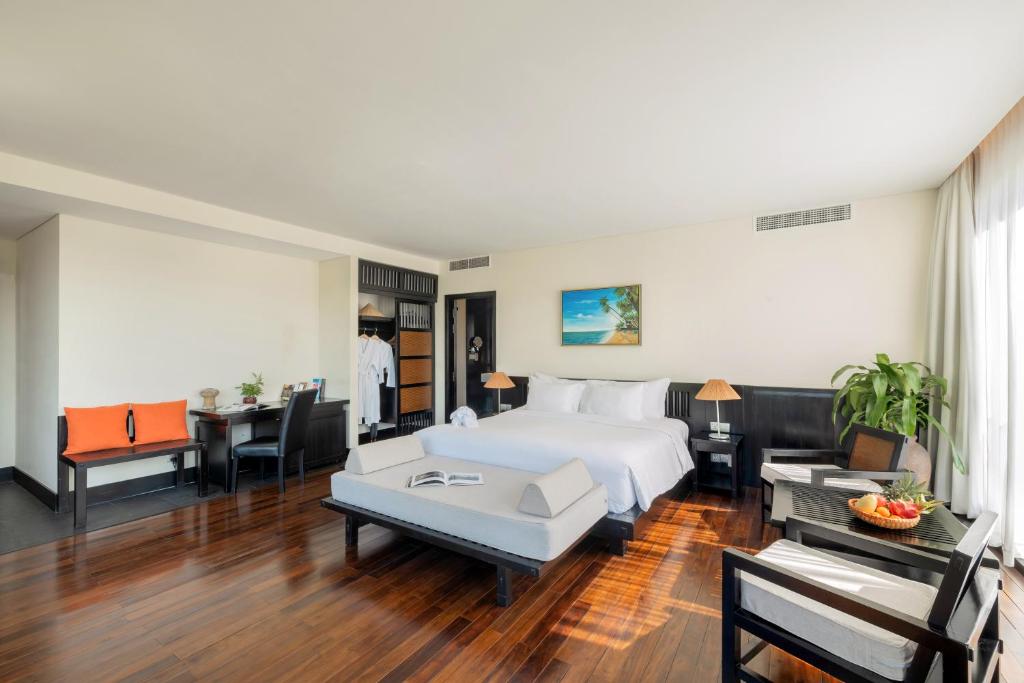 Moderns viesnīcas numurs ar koka grīdu, plašu gultu un mājīgu atpūtas stūrīti. Interjerā ir galda zona un attēls ar pludmali uz sienas.