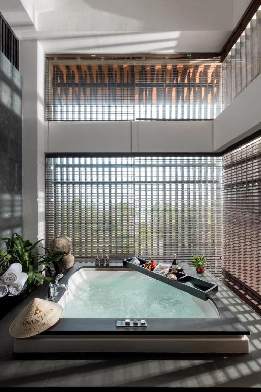 Mūsdienīgs vannas istabas interjers ar modernu džakuzi, kas ir aprīkots ar augstām logu konstrukcijām, caur kurām ieplūst dabiska gaisma. Blakus atrodas dekoratīvas augu kompozīcijas un relaksējoši piederumi.