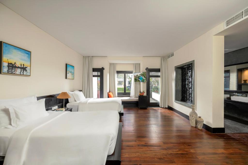 Moderns viesnīcas numurs ar divām gultām, koka grīdu un dabīgu apgaismojumu, kas rada mājīgu atmosfēru. Logi sniedz skatu uz dārzu un ir rotāti ar gaisīgām aizkariem.